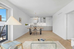 Una cocina moderna con armarios blancos, un comedor con mesa y sillas, y un amplio ventanal que proporciona luz natural.