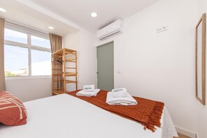 Ett hotellrum med en säng, en hylla i trä, en luftkonditioneringsanläggning och utsikt över omgivningarna.