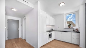 Eine moderne Küche mit weißen Schränken, einem Einbauofen, einem Spülbecken und einem Fenster mit Blick auf die Stadt.