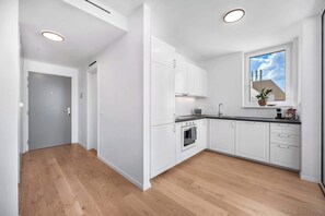A modern kitchen with white cabinets, a built-in oven, a sink, and a window with a cityscape view.