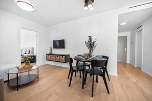 A modern living room with a dining area, wooden flooring, a flat-screen TV, and a minimalist decor.