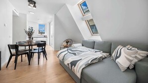 Ein modernes Schlafzimmer im Loft-Stil mit schrägem Dach, integriertem Bett, Essbereich und Blick durch ein Dachfenster.