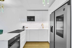 Una cocina moderna con armarios blancos, horno empotrado, refrigerador de acero inoxidable y piso de madera.