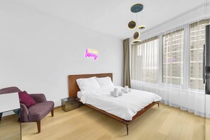A modern hotel room with a bed, a chair, a desk, and a window with curtains.