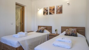 A hotel room with two beds, a wooden headboard, a small bedside table with a plant, and artwork on the wall. - S 03 - 1 Bed Flat in Quinta São Silvestre (Lagos)