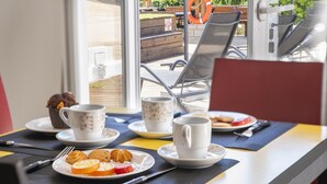A breakfast setup with plates of pastries, a coffee cup, and a muffin on a table with a view of outdoor seating. - S 03 - 1 Bed Flat in Quinta São Silvestre (Lagos)