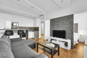 Ein modernes Wohnzimmer mit Sofa, Couchtisch, Fernseher und einer Küche im Hintergrund.