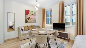 A modern living room with a round dining table, sofa, TV, and a large window with curtains. - On the Main Shopping Street - City Center (Bratislava)