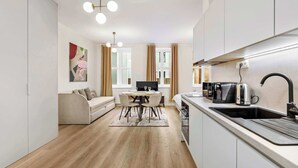 A modern kitchen with a dining area, a sofa, a TV, and a coffee machine. - On the Main Shopping Street - City Center (Bratislava)