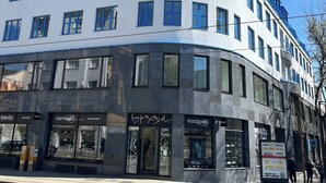 A multi-story building with a curved facade, storefronts on the ground floor, and a clear blue sky above. - On the Main Shopping Street - City Center (Bratislava)