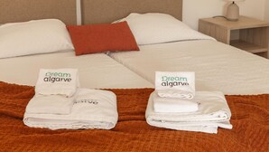 Habitación de hotel con una cama, dos almohadas, una mesita de noche con una lámpara y dos toallas dobladas con el texto 'Dream algarve'.