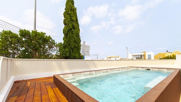 Tinaja rectangular con un muelle de madera, rodeada por una valla blanca y un árbol alto al fondo.