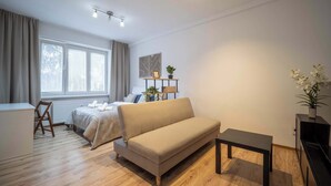 A modern bedroom with a sofa, a small table, a bed with a white headboard, a desk, and a window with curtains.