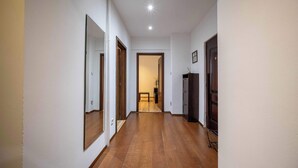 A hallway with wooden flooring, white walls, and a door leading to another room.