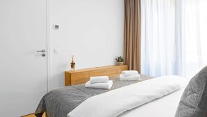 Hotellihuone, jossa on sänky, puinen pääty, ruukkukasvi ja ikkuna, jossa on verhot.