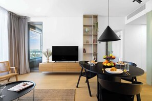 A modern living room with a dining table, a flat-screen TV, a bookshelf, and a large window. - Stylish Haven SkyPark Apartment (Bratislava - Old Town)