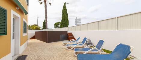 Una terraza en la azotea con sillones de descanso, una palmera y un alto pino.