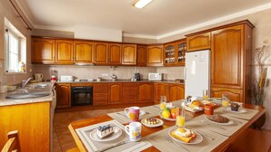 Una cocina con armarios de madera, un refrigerador y una mesa de comedor lista para el desayuno.
