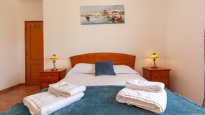 A hotel room with a bed, two bedside tables with lamps, a wooden wardrobe, and a painting on the wall. - L 03 - Bedroom 3 Western Mos Guesthouse (Lagos)