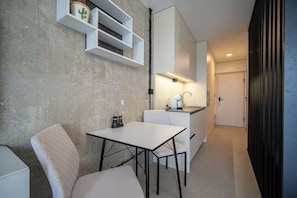 A compact kitchen with a white countertop, a built-in shelf, and a dining area with a table and chairs.