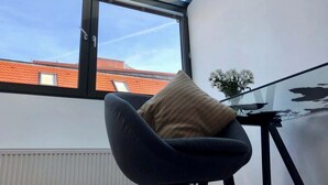 A room with a glass ceiling, a chair with a cushion, a small table, and a view of buildings outside. - Mi Apartments - Old Town Heart-Terrace&Castle View (Bratislava - Old Town)