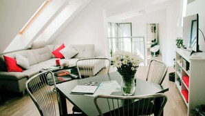 A modern living room with a dining table, chairs, a sofa, and a bookshelf. - Mi Apartments - Old Town Heart-Terrace&Castle View (Bratislava - Old Town)