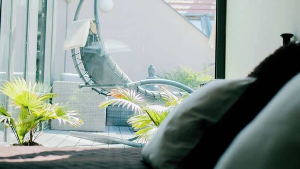 A modern interior with a large window, a unique chair, and small plants. - Mi Apartments - Old Town Heart-Terrace&Castle View (Bratislava - Old Town)