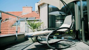 A modern balcony with a cushioned chair, glass doors, and a potted plant. - Mi Apartments - Old Town Heart-Terrace&Castle View (Bratislava - Old Town)