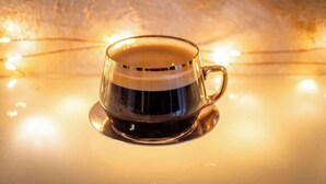 Una taza de vidrio transparente con asa, llena de un líquido oscuro, posiblemente café, sobre un platito.