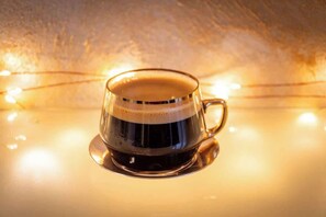 Eine transparente Tasse mit Henkel, gefüllt mit einer dunklen Flüssigkeit, vermutlich Kaffee, auf einem Untertasse.