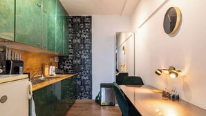 Una cocina compacta con un salpicadero decorado con motivos de café, un comedor con mesa y sillas, y un reloj montado en la pared.