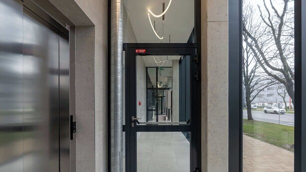 Una entrada moderna con puerta de vidrio, ascensor metálico y vista despejada a la calle.