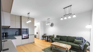 Una cocina moderna con armarios blancos, un área de comedor con un sofá verde y una mesa de centro de madera.