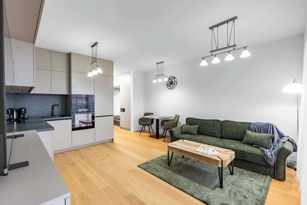 Eine moderne Küche mit weißen Schränken, ein Essbereich mit einem grünen Sofa und einem Holztisch.
