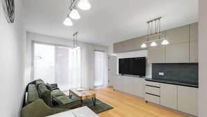 Una sala de estar moderna con sofá, mesa de comedor y área de cocina con armarios y televisor.