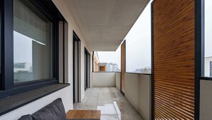 Un balcón estrecho con un banco de madera, un sofá y vistas de la ciudad.