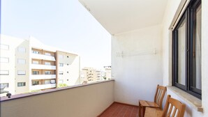 Un balcon avec deux chaises en bois, une fenêtre et une vue sur les immeubles voisins.