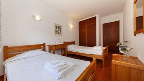 Une chambre d’hôtel avec deux lits en bois, une commode en bois, un miroir et un tableau encadré au mur.