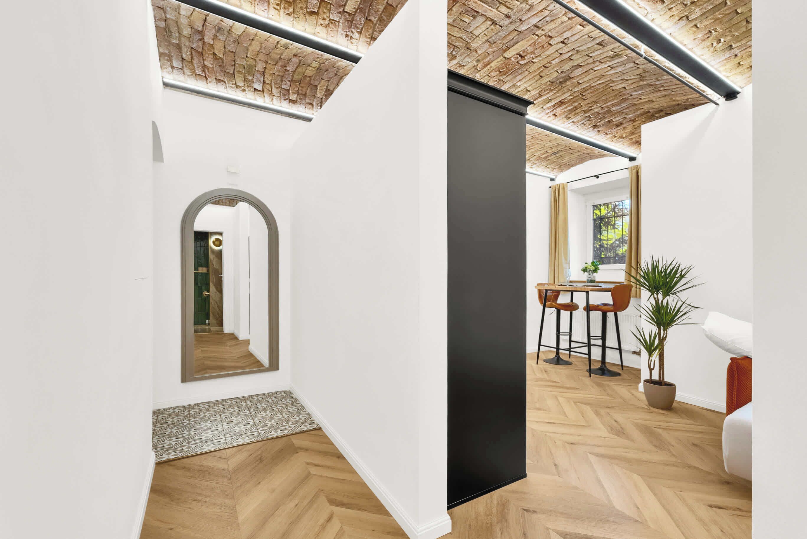 A modern interior with a herringbone wood floor, white walls, a black accent wall, and a brick ceiling.