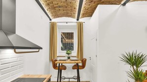 Una cucina compatta con fornelli moderni, una finestra con tende e un'area pranzo con sgabelli.