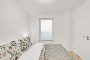 Un dormitorio con cama, ventana, radiador y puerta.