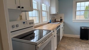 A kitchen with white cabinets, a built-in oven, a stove, a sink, and a window with curtains. - Lucky Horseshoe Farmhouse (Wilmington)