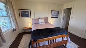 A bedroom with a bed, a nightstand, a lamp, a window with curtains, and two framed pictures on the wall. - Lucky Horseshoe Farmhouse (Wilmington)