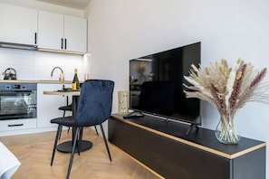 Una cuina moderna amb televisió de pantalla plana, zona de menjador amb una cadira fosca i un ram de flors seques.