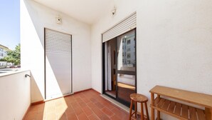 Un balcon avec un banc en bois, une porte coulissante et une vue sur un immeuble.