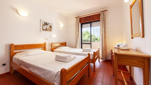 Une chambre d’hôtel avec deux lits en bois, un bureau, un miroir et une fenêtre avec des rideaux.