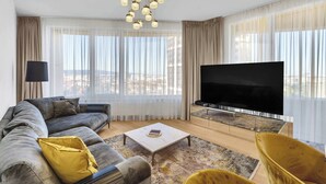 Ein modernes Wohnzimmer mit einer Couch, einem Couchtisch, einem Fernseher und großen Fenstern.