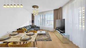 Ein modernes Wohnzimmer mit Essbereich, einer Couch, einem Fernseher und großen Fenstern.