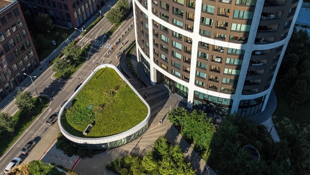 Ein Hochhaus mit einem gewölbten, grünen Dachgarten, einer geschwungenen Auffahrt und einem Fußgängerweg.