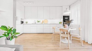 Une cuisine moderne avec des meubles blancs, un coin repas doté d’une table ronde et de chaises, et une plante en pot.